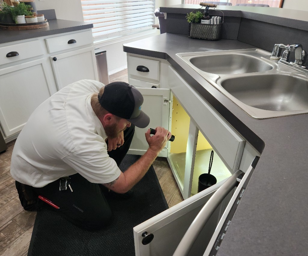 Everflow technician inspecting kitchen sink plumbing inside a customer cabinet