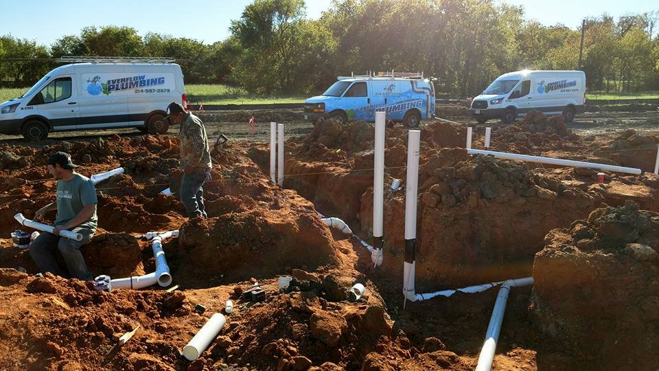 Everflow Plumbing new construction crew installing underground PVC drainage with fleet vans on site